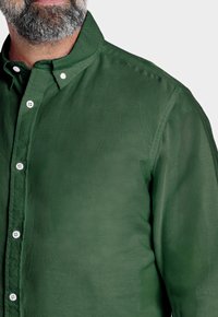 Camisa verde de botones con cuello, hecha de un tejido texturizado. Presenta botones blancos y un diseño moderno y relajado.