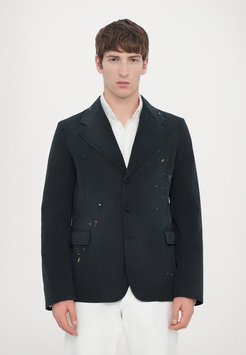 Blazer de algodón negro con un corte entallado, que presenta un solapa con muesca, tres botones y salpicaduras de pintura coloridas en la parte delantera.