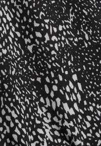 Gros plan d’un tissu noir avec des taches blanches irrégulières créant un motif abstrait et dispersé sur la surface.