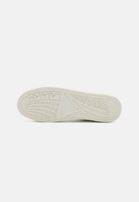 Semelle de chaussure en caoutchouc blanc avec des motifs texturés, présentant des lignes diagonales et un design de semelle en forme d'étoile pour une meilleure adhérence.
