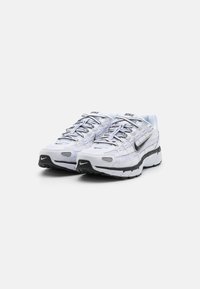 Pantofi de alergare Nike cu un brâu din plasă albă, accente negre și o talpă cu un model. Dispun de șireturi, toc cu amortizare și logo pe lateral.
