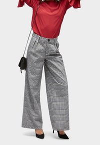 Pantalons large à carreaux gris et noirs avec une taille haute, des plis à l'avant et une coupe décontractée, associés à un haut rouge et des talons noirs.