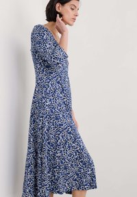 Niebieska sukienka w biały kwiatowy wzór, do długości midi, z okrągłym dekoltem i rękawami o długości trzy czwarte, wykonana z miękkiego materiału.