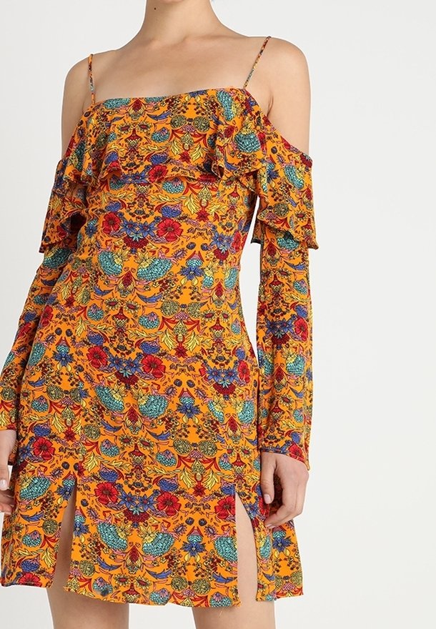 Vestido sin hombros de vibrante tela naranja, con patrones florales en rojo y verde, detalles con volantes y aberturas laterales.