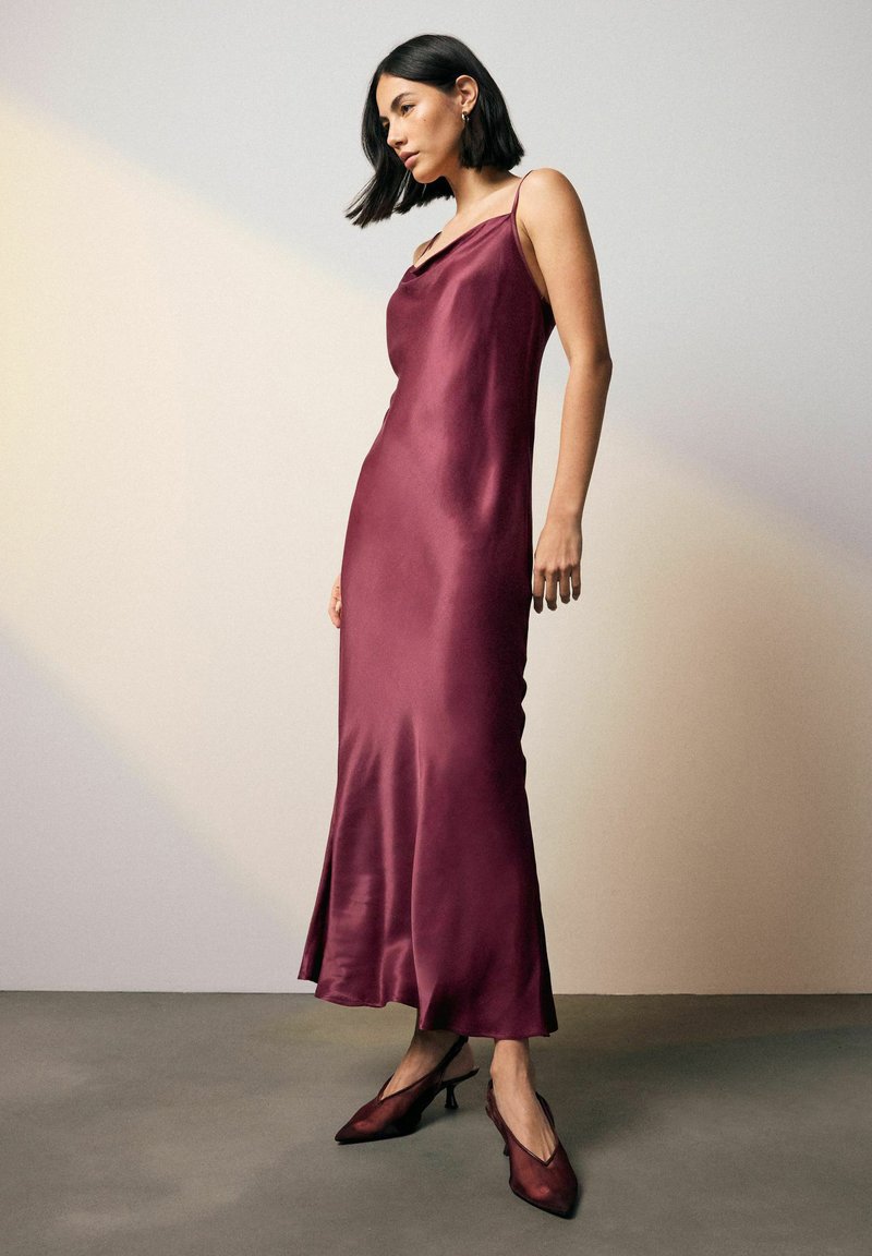 Burgundy satiinimekko, jossa on laskostettu pääntie, sulava siluetti ja nilkkapituisuus. Yhdistetty samanväristen burgundinpunaisiin slingback-korkokenkiin.