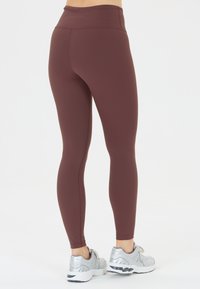 Vinröda leggings med hög midja, slät textur och en figursydd passform. Bärs med silverfärgade sportskor för stil.