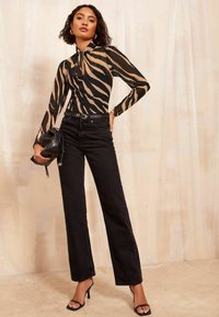 Jeans neri a vita alta abbinati a una blusa trasparente a maniche lunghe con stampa zebra beige e nera, completati da una borsa nera.