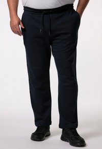 Pantalones de chándal azul marino con cinturilla ajustable, bolsillos laterales y perneras ajustadas, complementados con zapatillas deportivas negras. Textura de tela suave.