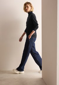 Svart polo-tröja i texturerad tyg, matchad med mörkblå raka jeans och vita sneakers, som visar upp avslappnad komfort.