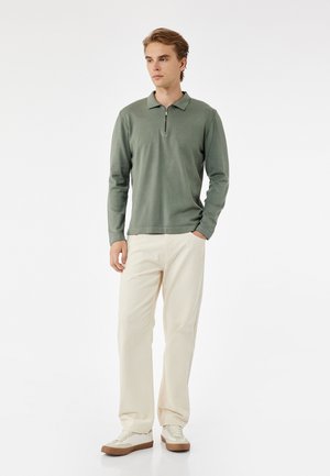 Lichtgroene lange mouwen polo met een kwart rits kraag, gecombineerd met crèmekleurige broek en witte sneakers met bruine zolen.