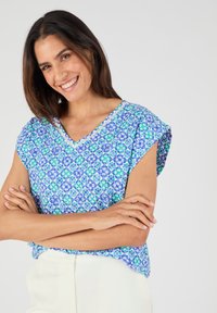 Blusa a maniche corte blu e verde con motivo a fantasia e scollatura a V. Tessuto leggero con motivi floreali e dettagli in pizzo.