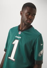 Eagles NFL trøje i grøn og sort, med det store hvide nummer "1," logo detaljer på ærmerne, og v-hals design.