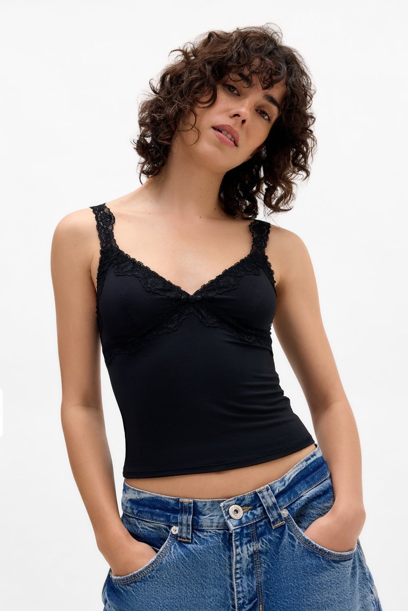Black tank top with lace trim, featuring adjustable straps, a v-neck, and a fitted silhouette. Paired with high-waisted denim shorts.