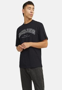 Sort bomuld t-shirt med hvidt "JACK & JONES" tekst og buet detaljering. Korte ærmer og en klassisk pasform.