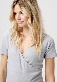 Grå ribbet kortærmet top med en omslagssilhuet, der har en dyb V-udskæring og blød tekstur, båret af en model med bølget blond hår.
