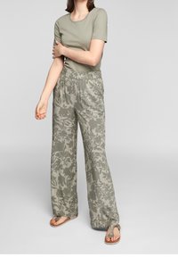 T-shirt vert olive clair associé à un pantalon large à motifs avec un design floral dans une palette de couleurs similaire. Porté avec des sandales beige.