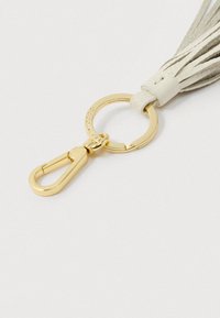 Złoty brelok z zapięciem przymocowany do beżowego chwosta z zamszu na białym tle.