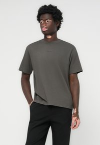 Dark gray short-sleeve t-shirt made of soft cotton, featuring a crew neckline and a small logo printed near the collar. Worn with black pants.