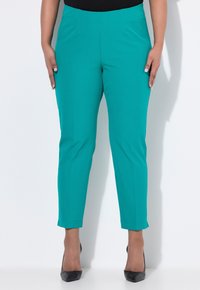 Tyrkysové slim-fit kalhoty s hladkou texturou, zkrácenou délkou ke kotníkům a čistým designem pasu. V kombinaci s černými lodičkami na vysokém podpatku.