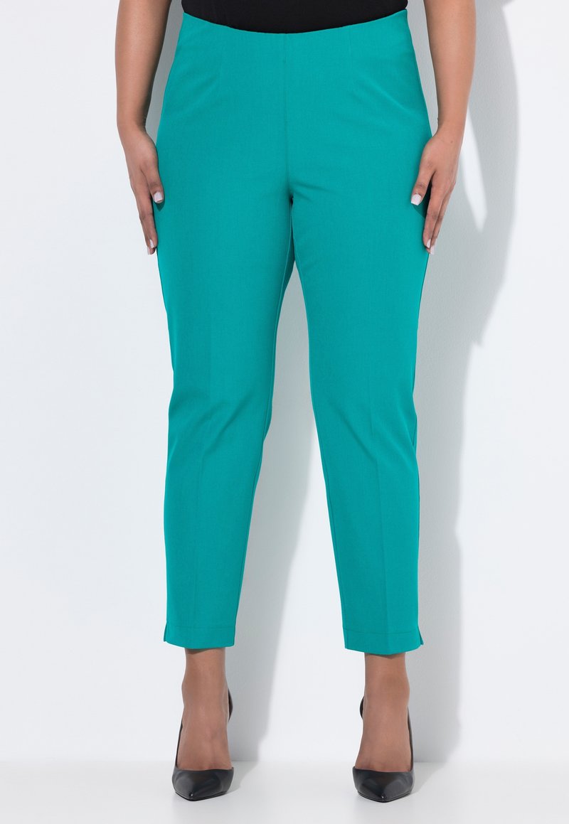 Tyrkysové slim-fit kalhoty s hladkou texturou, zkrácenou délkou ke kotníkům a čistým designem pasu. V kombinaci s černými lodičkami na vysokém podpatku.
