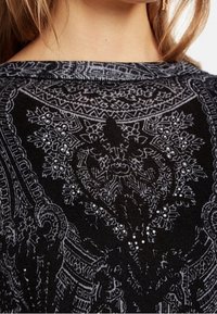 Schwarzes Oberteil mit komplexen grauen Mustern und Verzierungen, aus einem strukturierten Strickstoff. Subtiler Glanz durch dekorative Details.