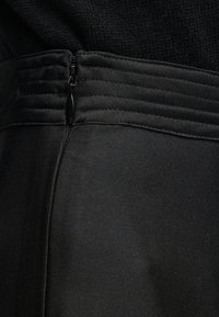 Κοντινό πλάνο μαύρου ενδύματος με κάθετη ραφή και κλειστό φερμουάρ κοντά στη υφασμάτινη ζώνη με υφή.