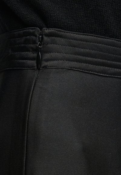 Zbliżenie czarnego ubrania z pionowym szwem i zamkniętym zamkiem błyskawicznym przy fakturowanym pasku w talii.