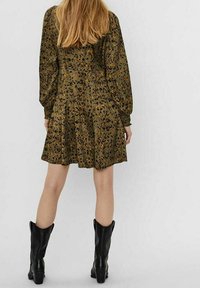 Blommönstrad klänning i mörkgrön, med långa ärmar och en utsvängd kjol. Matchas med höga svarta läderstövlar.