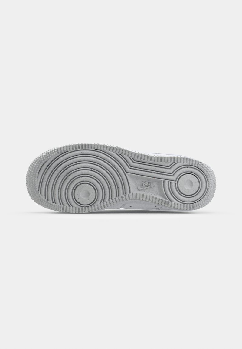 Semelle de sneaker en caoutchouc gris avec des textures circulaires et linéaires, présentant des sections en creux et un logo. Matériau lisse et durable avec des motifs de traction.