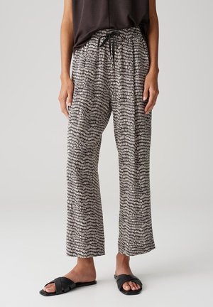 Persona que lleva pantalones holgados con estampado en blanco y negro con cordón negro, top sin mangas negro y sandalias negras planas.