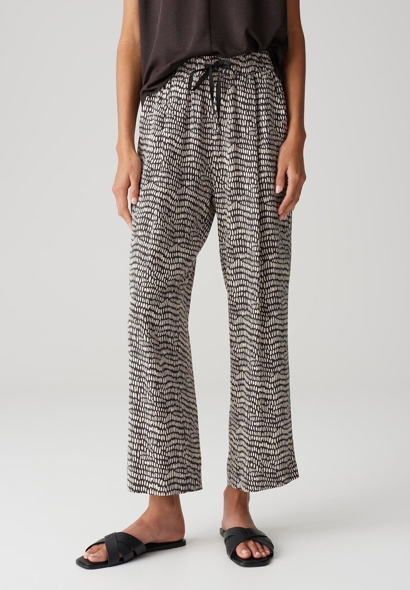 Personne portant un pantalon ample à motifs noir et blanc avec un cordon noir, un haut noir sans manches et des sandales plates noires.