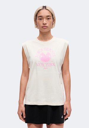 Person med kort blondt hår iført hvid ærmeløs top med pink "ASICS Tennis New York" print og sort nederdel, stående mod en ensfarvet baggrund.