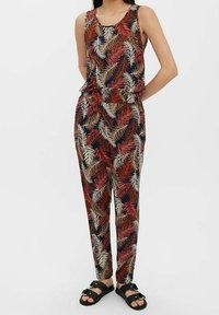 Bodysuit à motifs floraux avec un haut sans manches et un pantalon fuselé dans des tons naturels de rouge, crème et marine, fabriqué à partir d'un tissu léger.