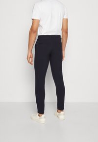 Marinblå figurnära byxor med en slät yta, utrustade med bälteöglor och två bakfickor. Bärs med en enkel vit t-shirt och vita sneakers.