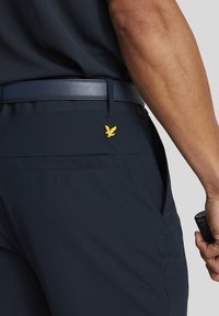 Marineblau Hosen aus leichtem Stoff, mit einer Gesäßtasche, einem gestickten gelben Vogel-Logo und einem glatten schwarzen Gürtel.