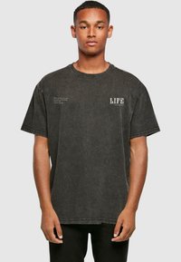 Sort oversized t-shirt med rund hals, med trykt tekst på forsiden. Materialet ser blødt ud med en falmet tekstur.