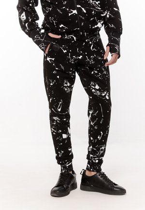 Czarne spodnie dresowe z białym wzorem w plamki, wykonane z teksturowanej tkaniny, z elastycznymi ściągaczami i bocznymi kieszeniami, w połączeniu z czarnymi butami.