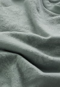 Ljust grönt tyg med en mjuk textur, med subtila nyansskillnader och en svag lyster, draperat i veck.