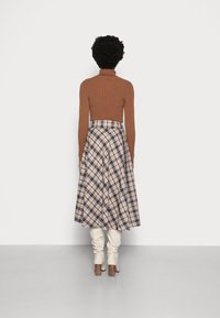 Brauner gerippter Rollkragenpullover kombiniert mit einem karierten A-Linien-Rock in Beige-, Braun- und Schwarztönen, ergänzt durch cremefarbene knielange Stiefel.