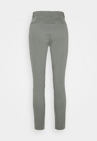 Pantaloni slim fit in tessuto grigio chiaro, caratterizzati da una vita media, due tasche posteriori e una superficie liscia. Design minimalista senza fissaggi visibili.