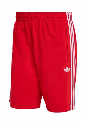 Czerwone krótkie spodenki sportowe z elastycznym pasem, białe paski po bokach oraz małe białe logo na lewej nogawce. Gładka faktura materiału.