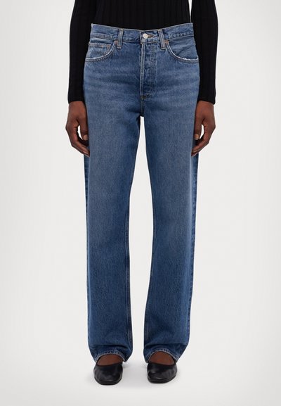 Jean en denim bleu à jambe large avec taille haute, design à cinq poches et décoloration subtile. Comprend des accessoires en laiton et une coupe droite.