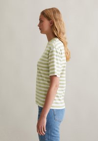 T-shirt à manches courtes rayé en vert clair et blanc, fabriqué en coton doux. Il présente un col ras du cou classique et une coupe décontractée.