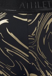 Schwarze sportliche Leggings mit einem strukturierten, gemusterten Design in Gold und einem schwarzen, markierten Bund. Das Material sieht dehnbar und glatt aus.