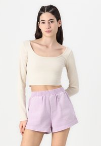Beige ribbet langærmet crop top parret med lyse lilla elastiske shorts med frontlommer og tekstureret stof.