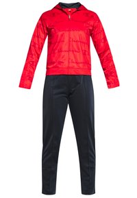 Veste rouge à fermeture éclair avec motif discret "Champion" en script, associée à un pantalon noir ajusté, présentée sur fond blanc.