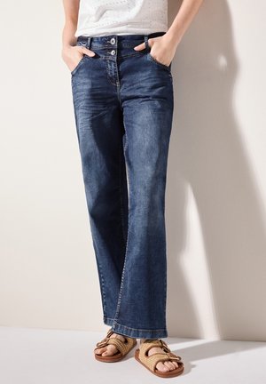 Wijdvallende donkerblauwe denim jeans hebben een knoopsluiting in de taille, twee voorzakken en een schone zoom. Gecombineerd met tangewebde sandals.
