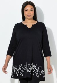 Schwarze Tunika mit Dreiviertelärmeln, V-Ausschnitt und weißem, besticktem Blumenmuster am Saum. Weicher, atmungsaktiver Stoff.