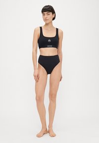 Sutiã desportivo preto e calções de biquíni de cintura alta com um logótipo circular na frente. Feito de material liso e elástico.