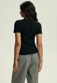 Czarna dopasowana koszulka z krótkim rękawem, z textured, prążkowanej tkaniny, zestawiona z czarno-białymi spodniami w kratkę w wysokim stanie.